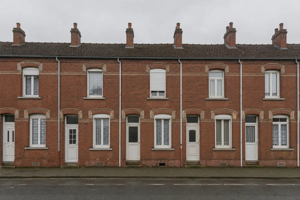 Rangée de maisons en brique rouge du Nord sous un ciel gris, cheminées alignées en toiture